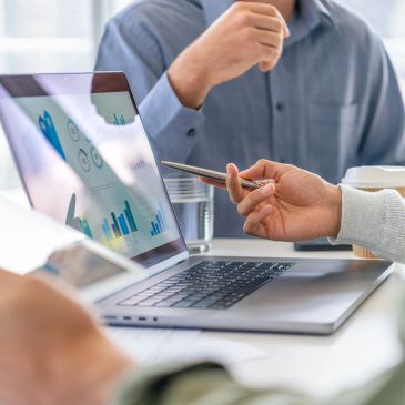 Business professionals discussing inventory management, demand forecasting, procurement data, operational KPIs, and supply chain analytics on a laptop to optimize cash flow, business performance, and operational efficiency.