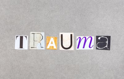Word "TRAUMA" spelled with cut-out letters on gray background.
