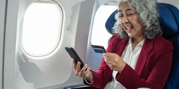 Smiling woman using phone and credit card on an airplane.