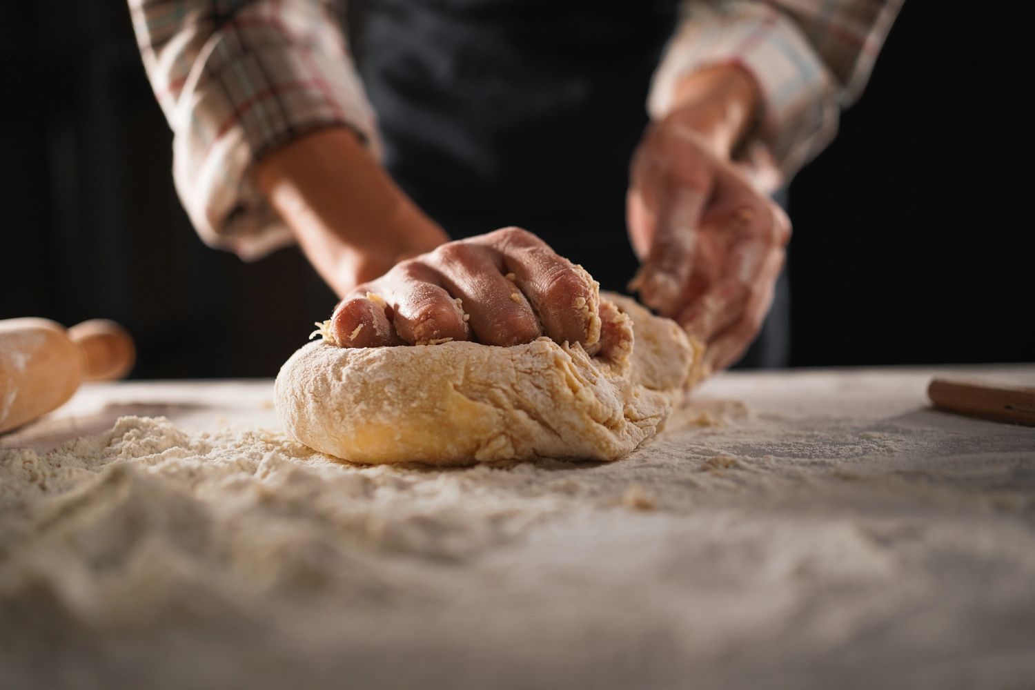 Hands kneading dough on a floured surface with a rolling pin nearby.
