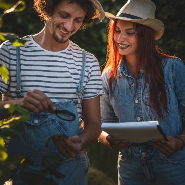 Two people examining plants outdoors with a notebook.