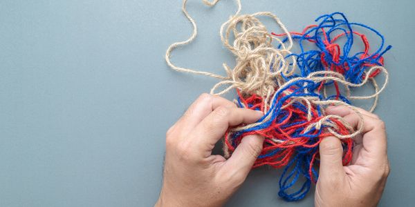 Two hands hold a tangle of three coloured yarns. 