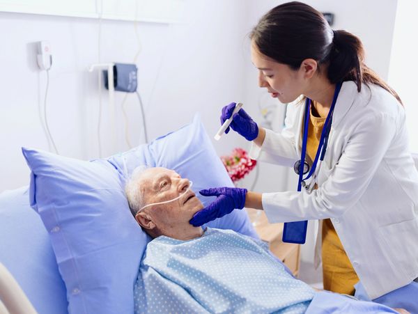 A doctor examines an elderly patient in a hospital bed.