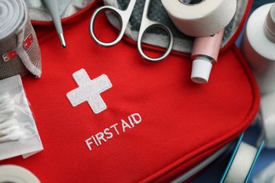 A red first aid kit with medical supplies on a surface.