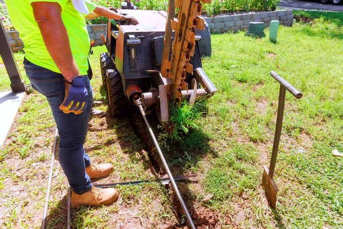 Worker with gloves operating a trenching machine in a grassy area.