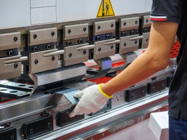 Worker operating a metal bending machine with gloved hand.