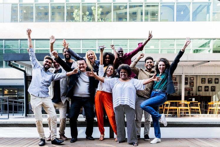 Happy diverse group celebrating with raised hands outdoors.