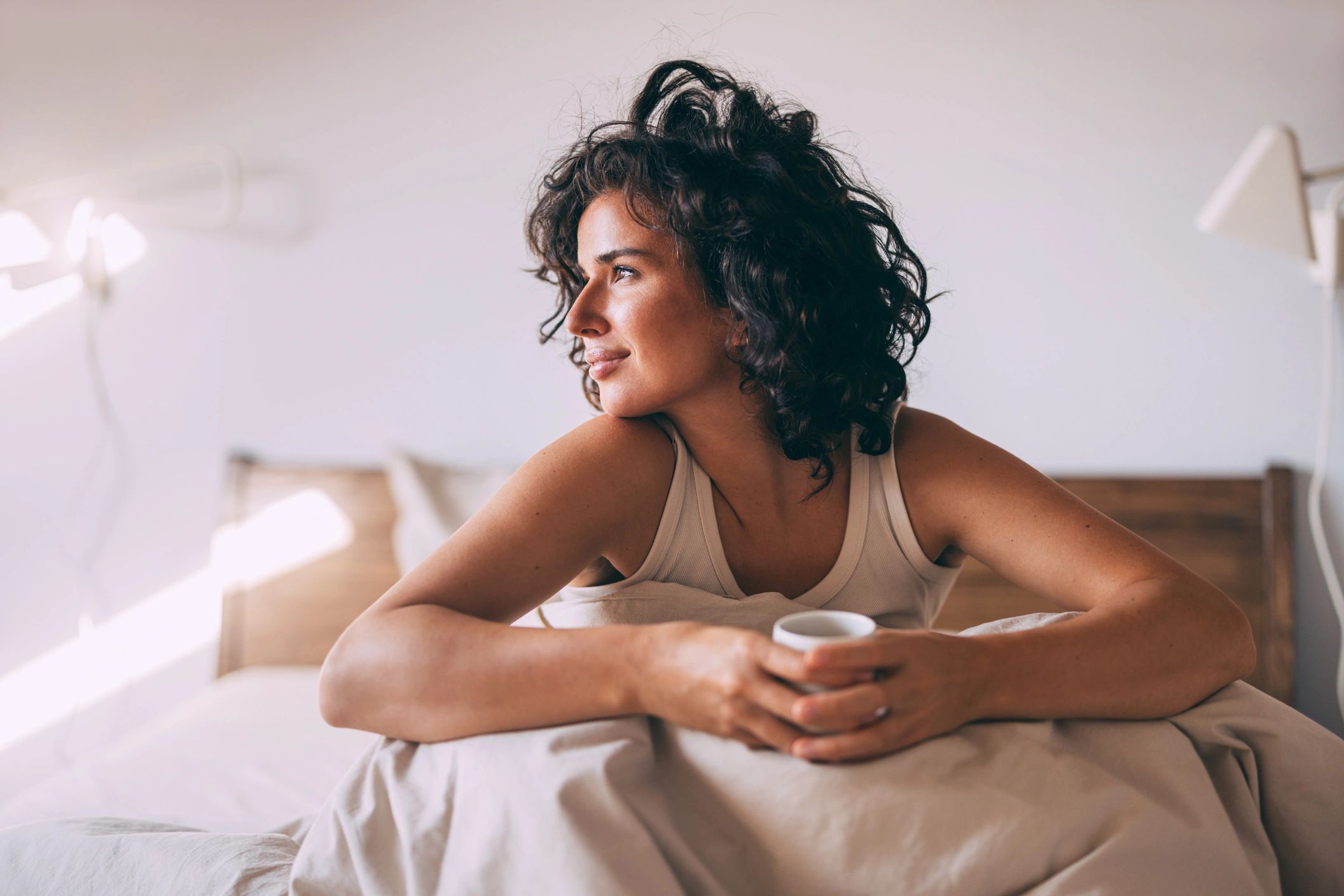 Woman with curly hair holding a cup, looking thoughtful.