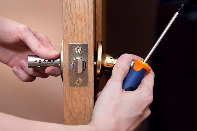 Door installation, worker Installs door knob, woodworker hands close up. A man spins the door handle with a screwdriver, repairs the door handle mechanism.