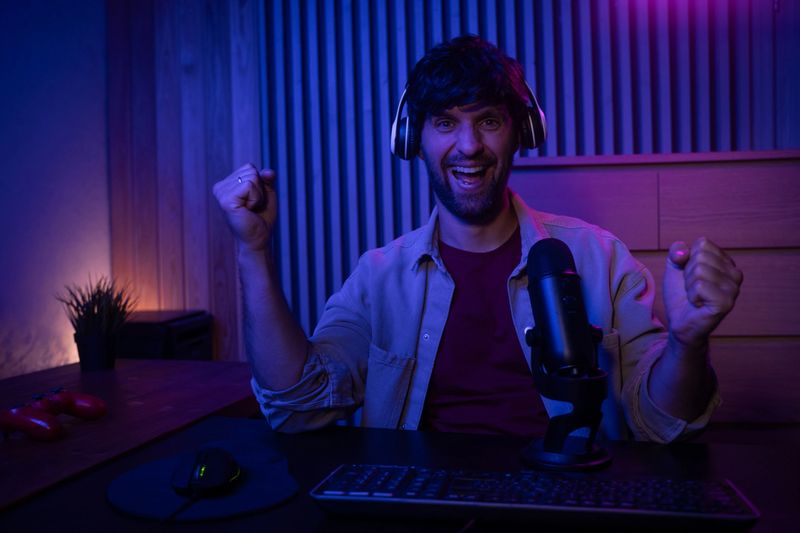 A gamer is actively participating in a live streaming session while speaking into a microphone. The setting features a stylish, dimly lit room with colorful lighting, creating an engaging atmosphere for viewers