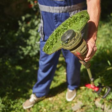 Person holding a grass-covered string trimmer in a garden.