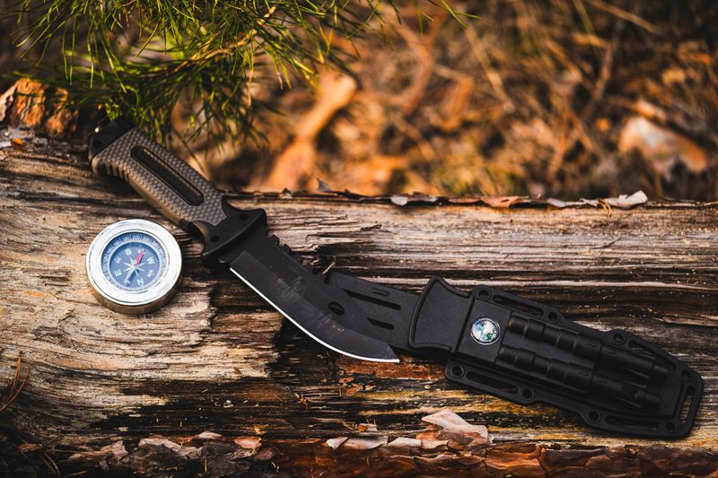 Hunting knife and compass on a log in the autumn forest