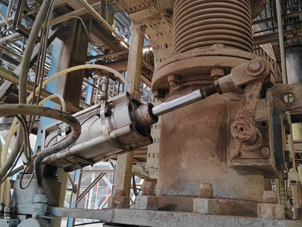 Industrial tie-rod hydraulic cylinder installed on heavy process equipment, used to move a large mec