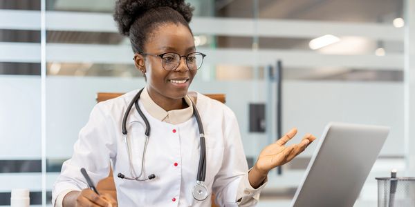 Smiling female doctor in white coat using laptop and taking notes.