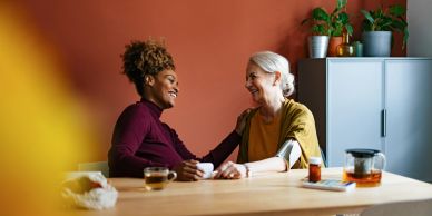 Twee vrouwen lachen en kletsen aan een tafel.