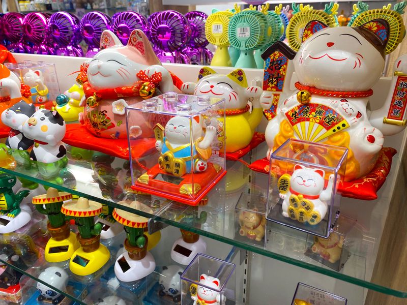 A display shelf in a shop featuring various lucky cat figurines and solar-powered toys.