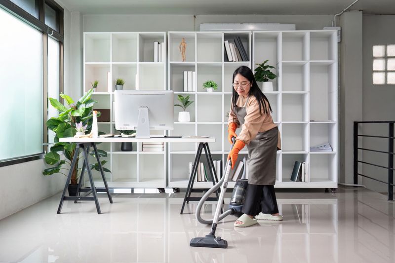 A professional maid or housekeeper cleaning a modern office space with a vacuum cleaner, ensuring a tidy and organized environment.