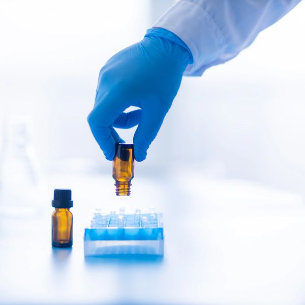 Gloved hand placing a small amber vial into a rack in a lab setting.