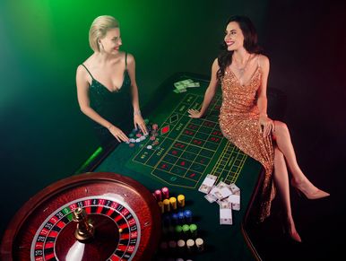 Two women in glamorous dresses enjoying a game at a casino roulette table.