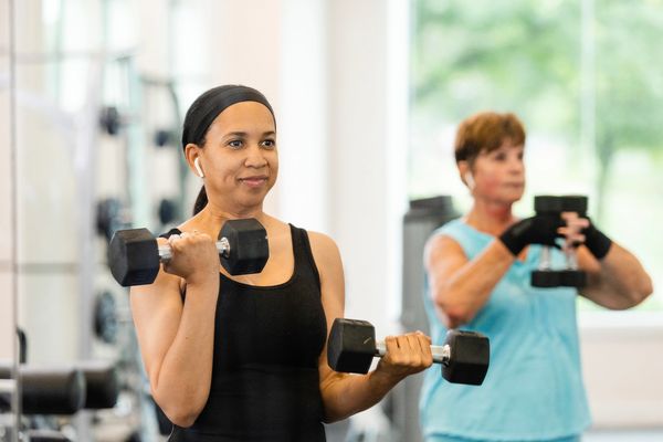 Two women lifting dumbbells in a gym, focused on their workout.