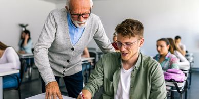 Older male teacher assisting a young male student in a classroom.