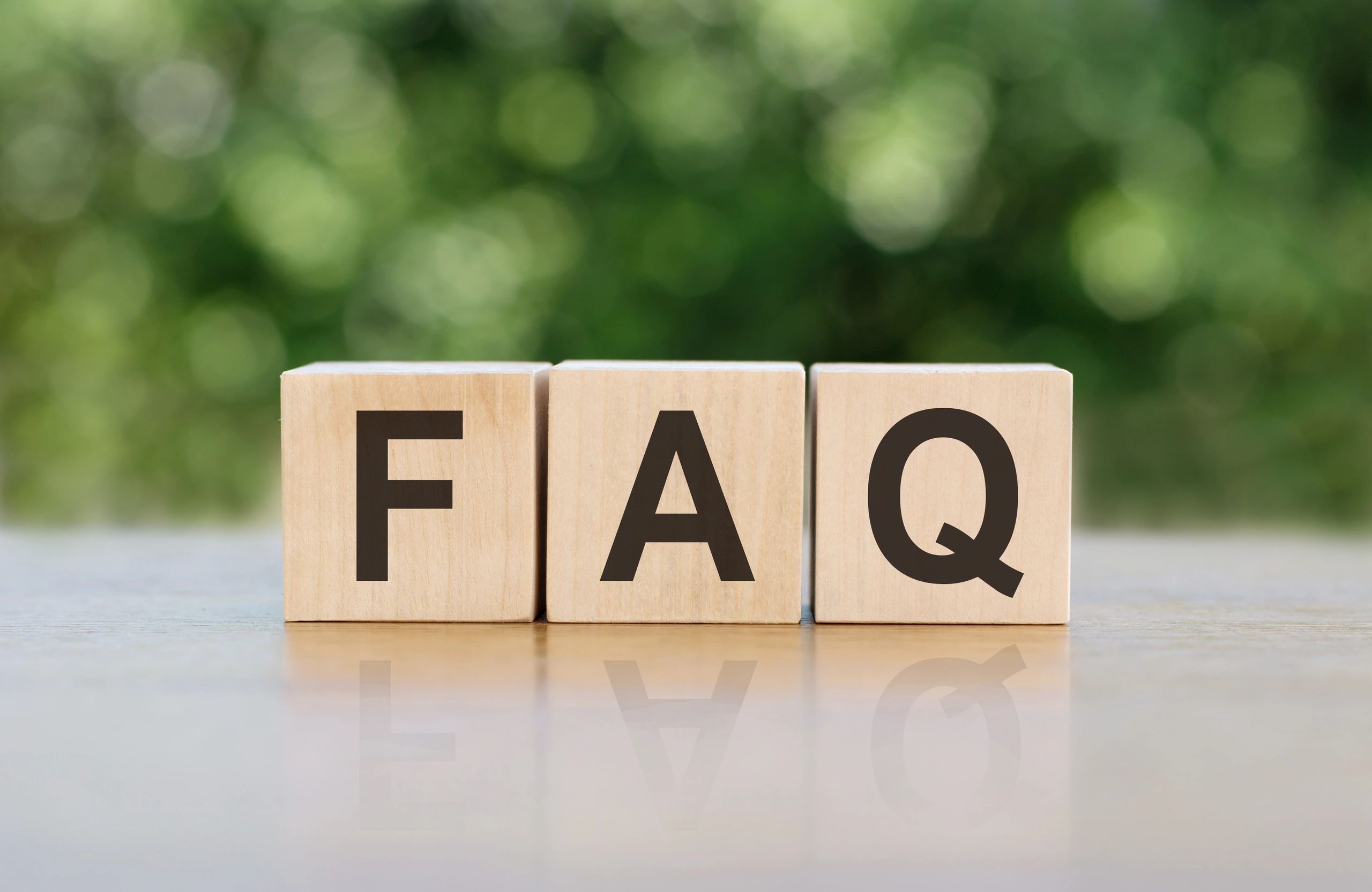 Frequently asked questions blocks on a flat surface with greenery in the back