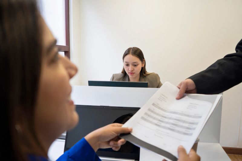 An older businessman, with gray hair and an experienced expression, reviews documents with his colleague in the office. Both are focused on the papers in front of them, discussing important details for a project. The interaction reflects a combination of wisdom and collaboration in a professional setting. both are dressed smartly.