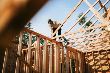 Construction worker installing wooden roof beams on a house frame.