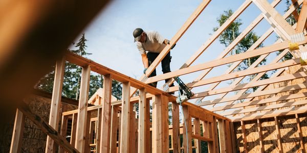 A construction worker installs wooden roof beams on a house frame.