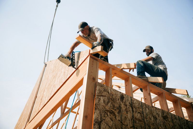 Workers build the frame of a new house project.  Bare plywood and beams as it is framed up from the foundation.  High lumber costs have affected the building process.  Shot in Washington state, USA.