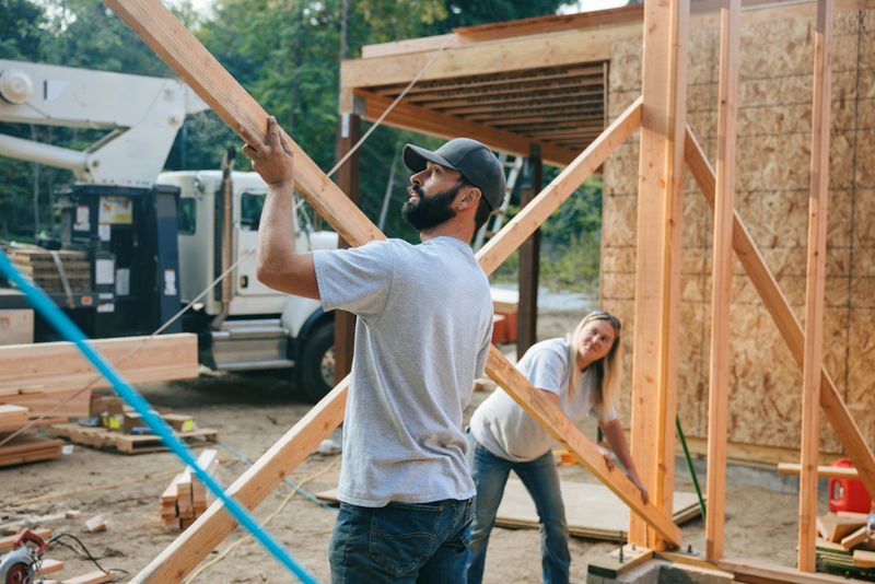 Workers build the frame of a new house project.  Bare plywood and beams as it is framed up from the foundation.  High lumber costs have affected the building process.  Shot in Washington state, USA.