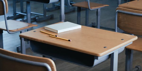 Empty classroom desk with a book and pencil.