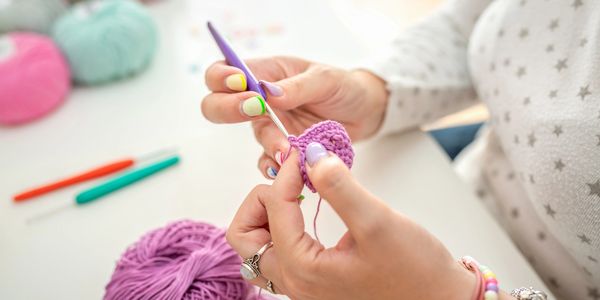 Close-up of hands crocheting with purple yarn and colorful nail polish.