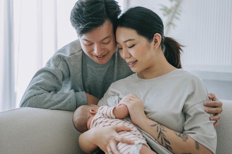 Asian Chinese young mother breastfeeding baby girl at home with father