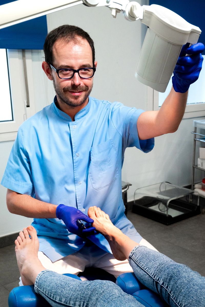 A podiatrist in a clinical setting is seen performing a foot examination on a patient. The podiatrist, wearing blue gloves and a medical uniform, is carefully attending to the patient's foot while adjusting a medical lamp for better visibility. The image highlights professional care, attention to detail, and the importance of hygiene and precision in podiatric treatments, capturing the essence of patient-centered healthcare