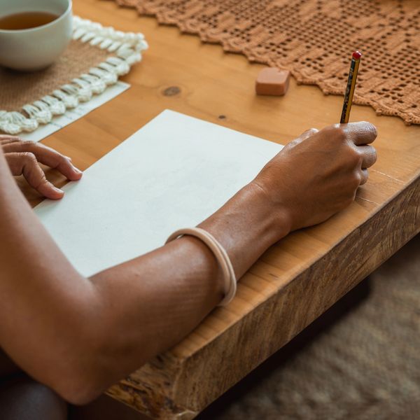 Person writing on blank paper at wooden table.