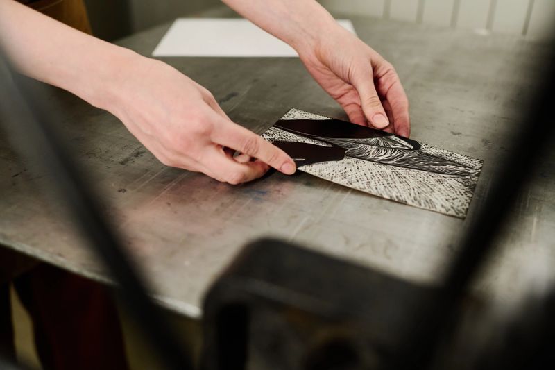 Hands of young unrecognizable female worker of typography house putting handmade artwork on steel tray of printing equipment