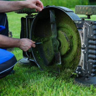 Person repairing the blade of a lawn mower on grass.