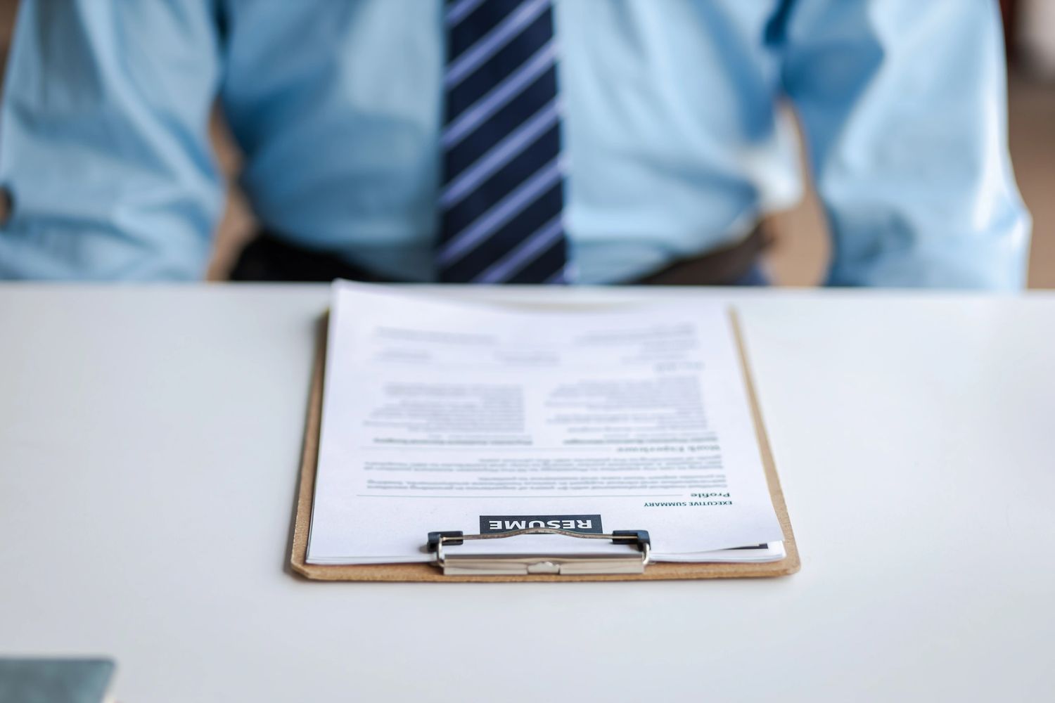 Person in a shirt and tie with a resume on a clipboard on the table.