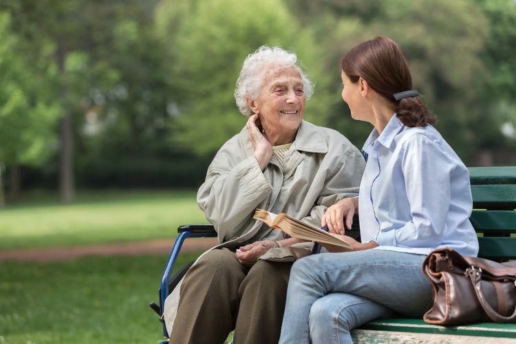 A young woman and an elderly woman share a joyful moment on a park bench.