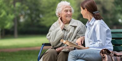 A young woman and an elderly woman share a joyful moment on a park bench.