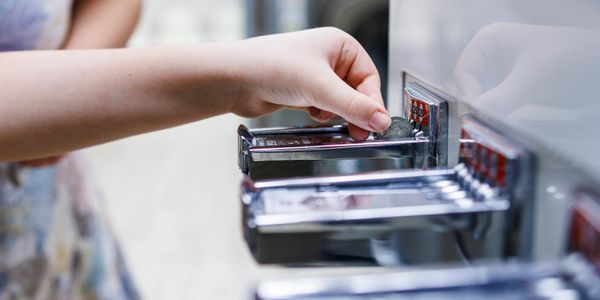 A hand inserting a coin into a vending machine's coin slot.