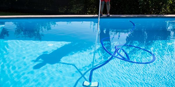 Person cleaning a swimming pool with a vacuum.