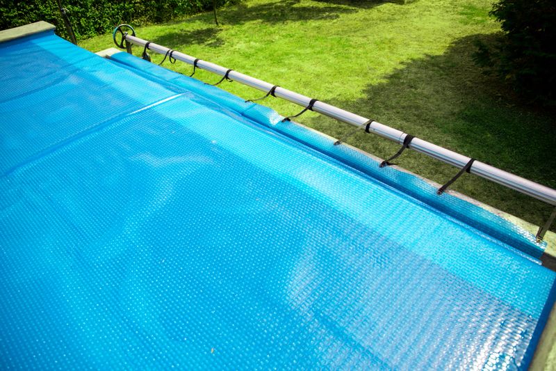 Part of blue solar pool cover floating on clean swimming pool. Keeping temperature and keeps clean the water