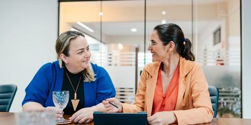 Two women in a meeting room engaged in a friendly conversation.