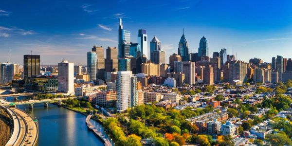 City skyline with river and vibrant greenery under blue sky.