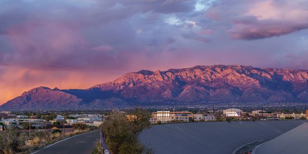 Sunset lights up mountains behind a cityscape with a cloudy sky.