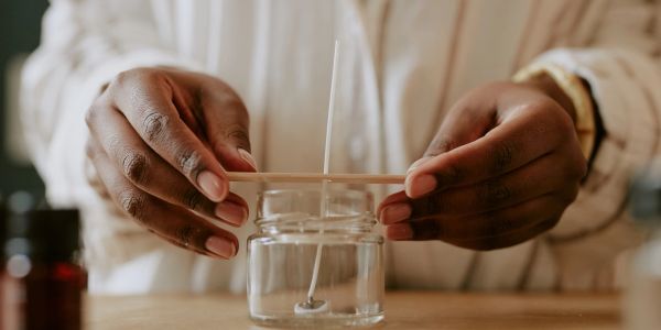 Person preparing a candle wick in a glass jar.
