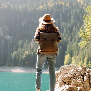 Person with backpack and hat overlooking a lake and forest.