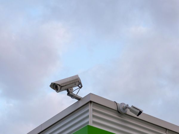 Two security cameras mounted on a building corner against a cloudy sky.